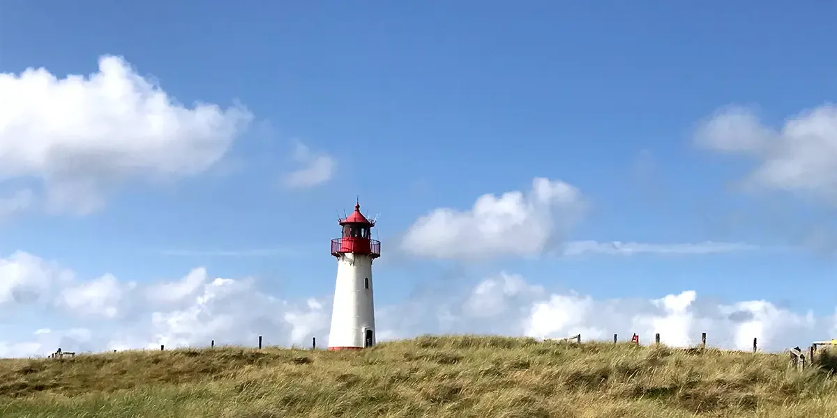 Weißer Leuchtturm mit rotem Top bei Tag auf Hügel mit Dünengras