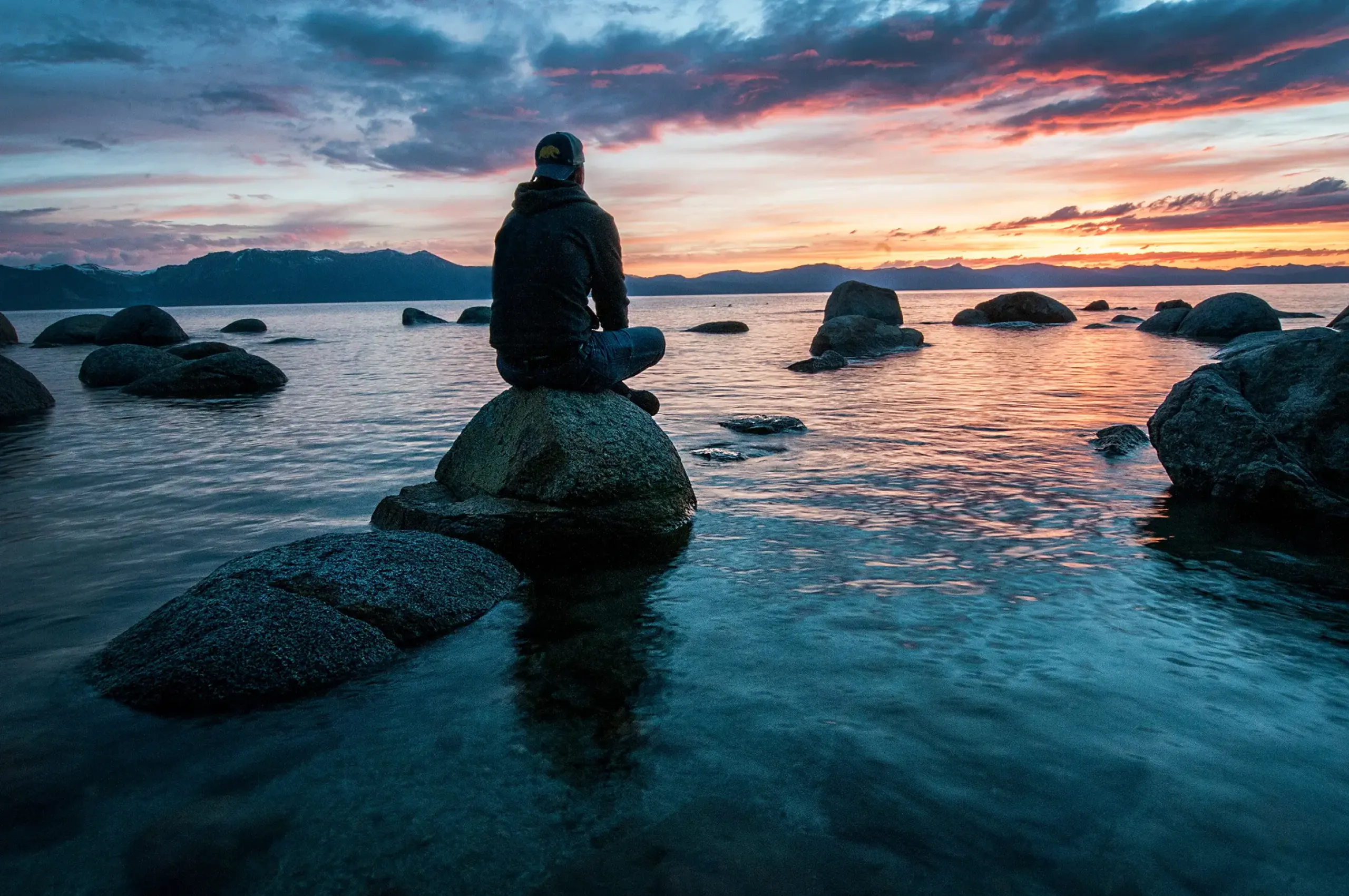 Mann sitzt auf Felsen am Strand und schaut aufs Meer